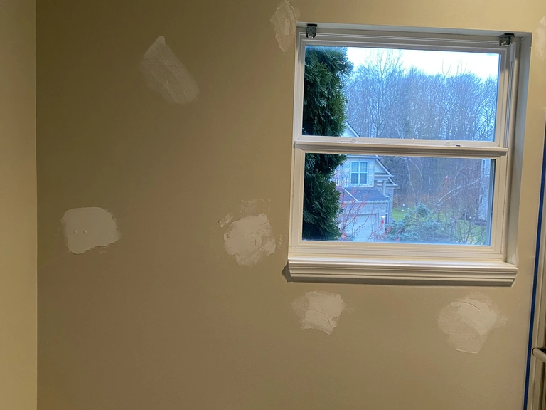 Spackled nail holes and dents around a window with a taping knife on the sill, drywall patching before paint in a Northeast Ohio home
