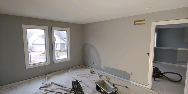 Prepped bedroom with a cut drywall opening awaiting its patch, drop cloths and tools on the floor, Aurora, Ohio