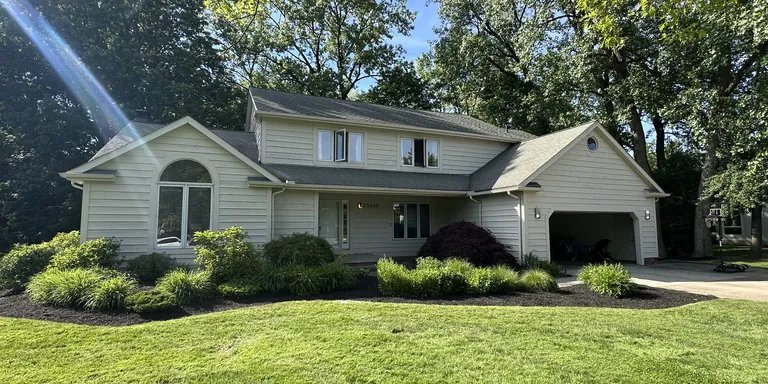 Cream two-story home with white trim and a landscaped front lawn, exterior painting