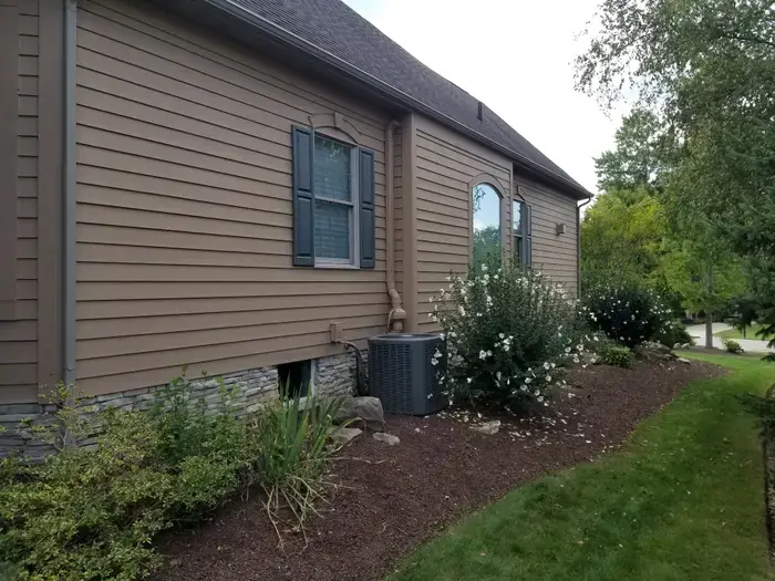 Tan vinyl siding with dark shutters after repainting on a Northeast Ohio home