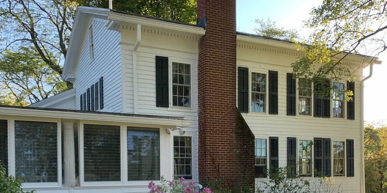 White farmhouse with black shutters and a brick chimney after exterior repainting in Chardon, Ohio
