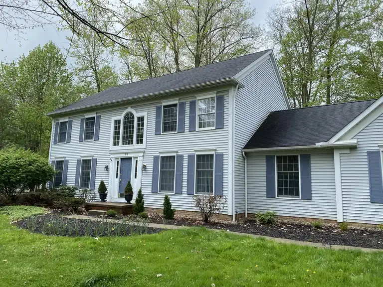 Two-story home with light blue siding, white trim and blue shutters freshly painted by Chagrin Falls Painting, Northeast Ohio