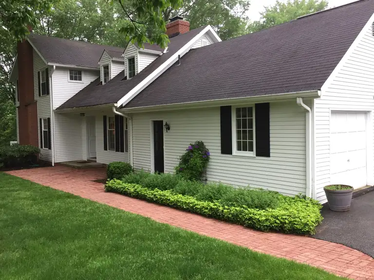 White cape-style home with black shutters and a red brick walkway after an exterior repaint, Northeast Ohio
