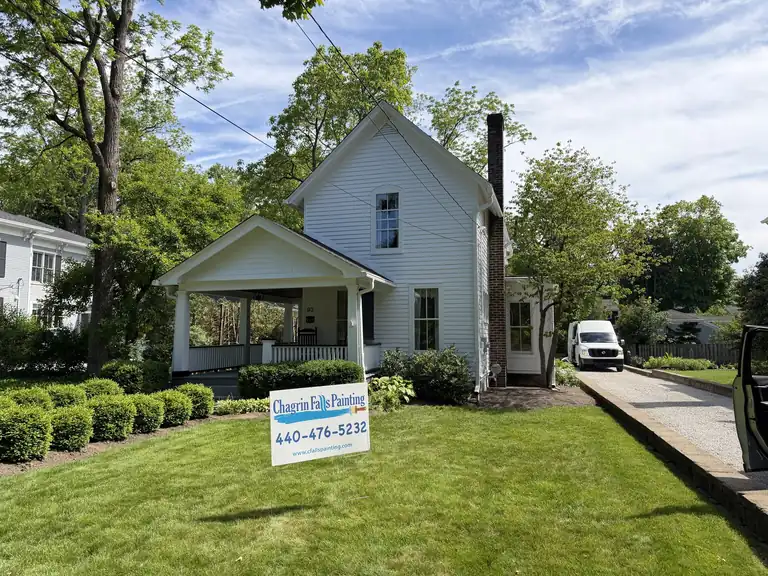 White farmhouse exterior freshly painted, with a Chagrin Falls Painting yard sign out front, Northeast Ohio