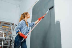 A homeowner using a paint roller to paint a wall, showcasing the effort required for DIY painting.