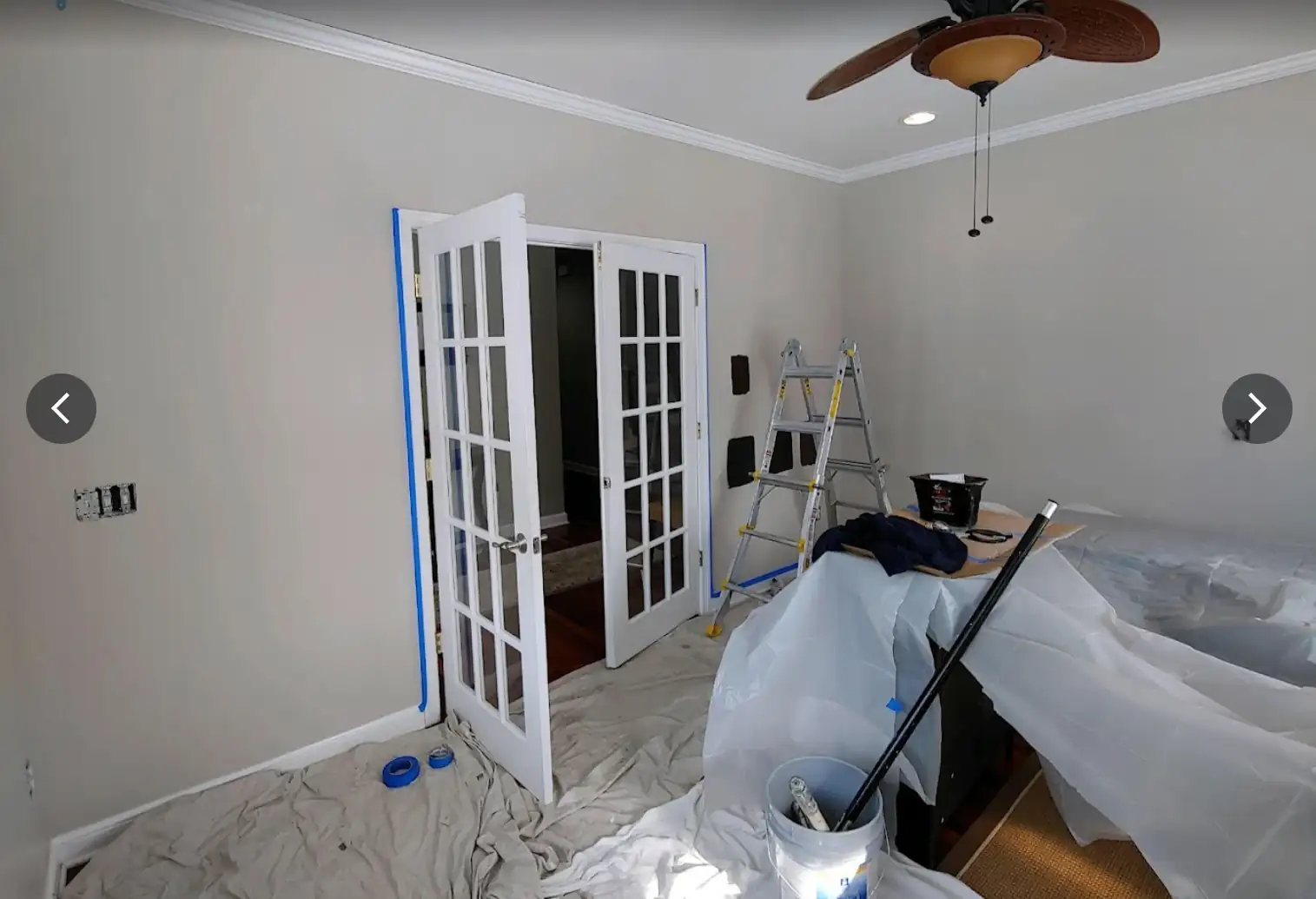 Interior residential painting prep with taped trim, protected floors, and covered furnishings for clean wall and ceiling work.