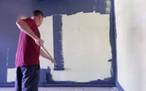 A man using a paint roller to carefully apply paint to a wall, demonstrating a key step in DIY house painting.