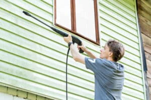 A man using a pressure washer to clean siding, preparing it for exterior painting in Cleveland's climate.