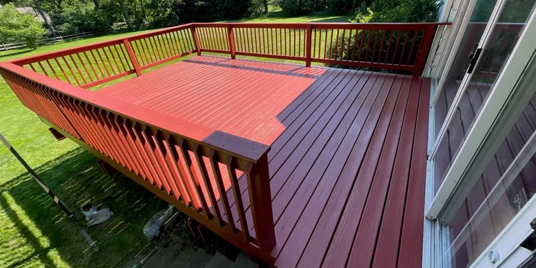 Backyard deck and railing painted a solid red beside the house