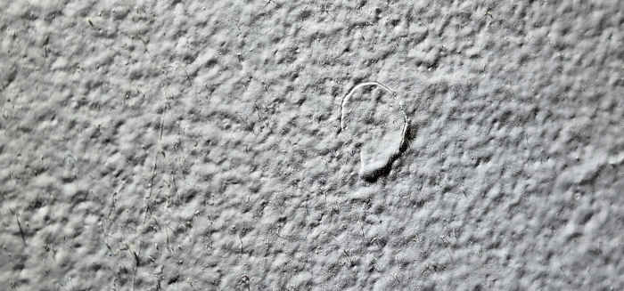 A single nail pop on drywall with subtle cracks forming around the protrusion.