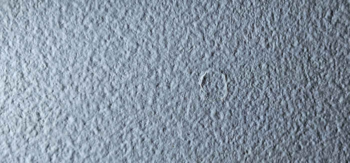 A single nail pop with slight paint flaking around the protrusion on drywall.