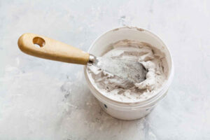 Small bucket of spackle with a putty knife placed inside