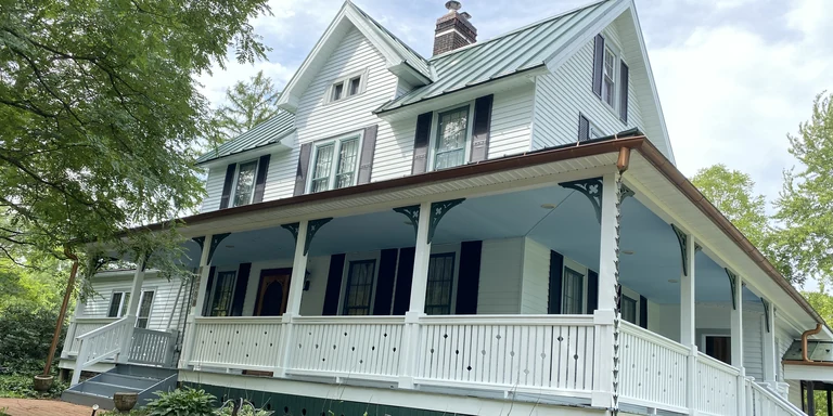 White Victorian home with a wraparound porch, black shutters and painted trim