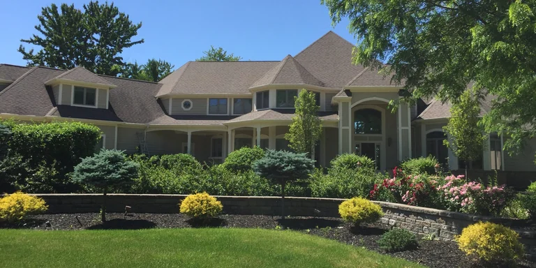 Tan two-story home with a wraparound porch after exterior painting in Aurora, Ohio